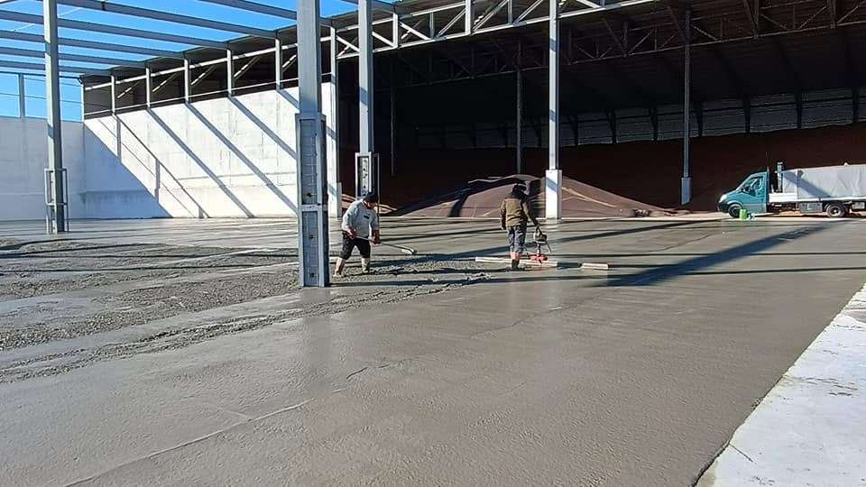 Echipă turnând și nivelând beton într-o hală în construcție