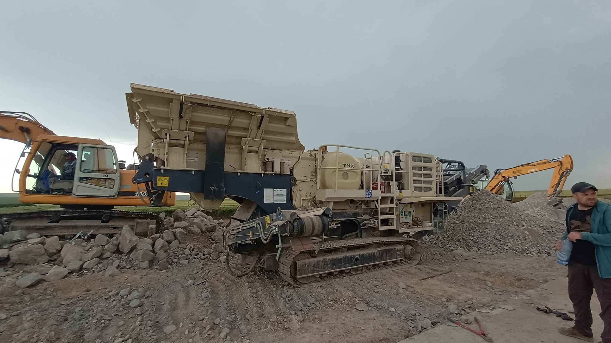 Excavator cu cupă alimentând concasorul mobil cu bucăți de beton