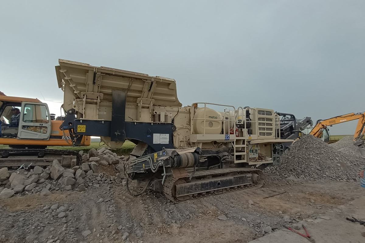 Excavator cu cupă alimentând concasorul mobil cu bucăți de beton