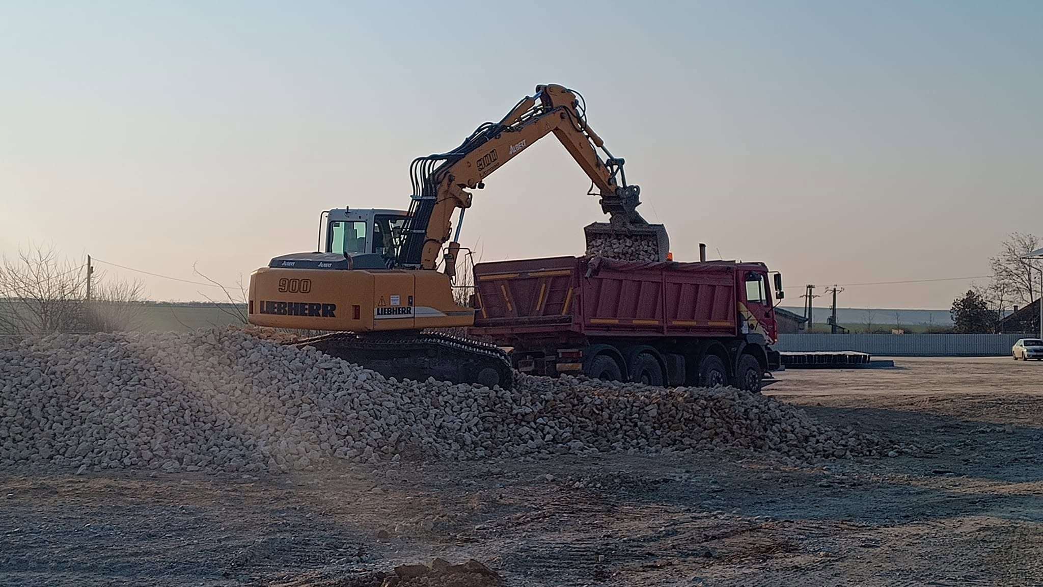 Autobasculantă încărcată de un excavator, la apus
