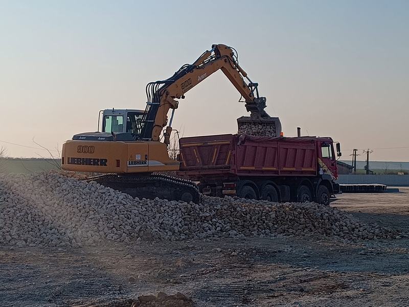 Autobasculantă încărcată de un excavator, la apus