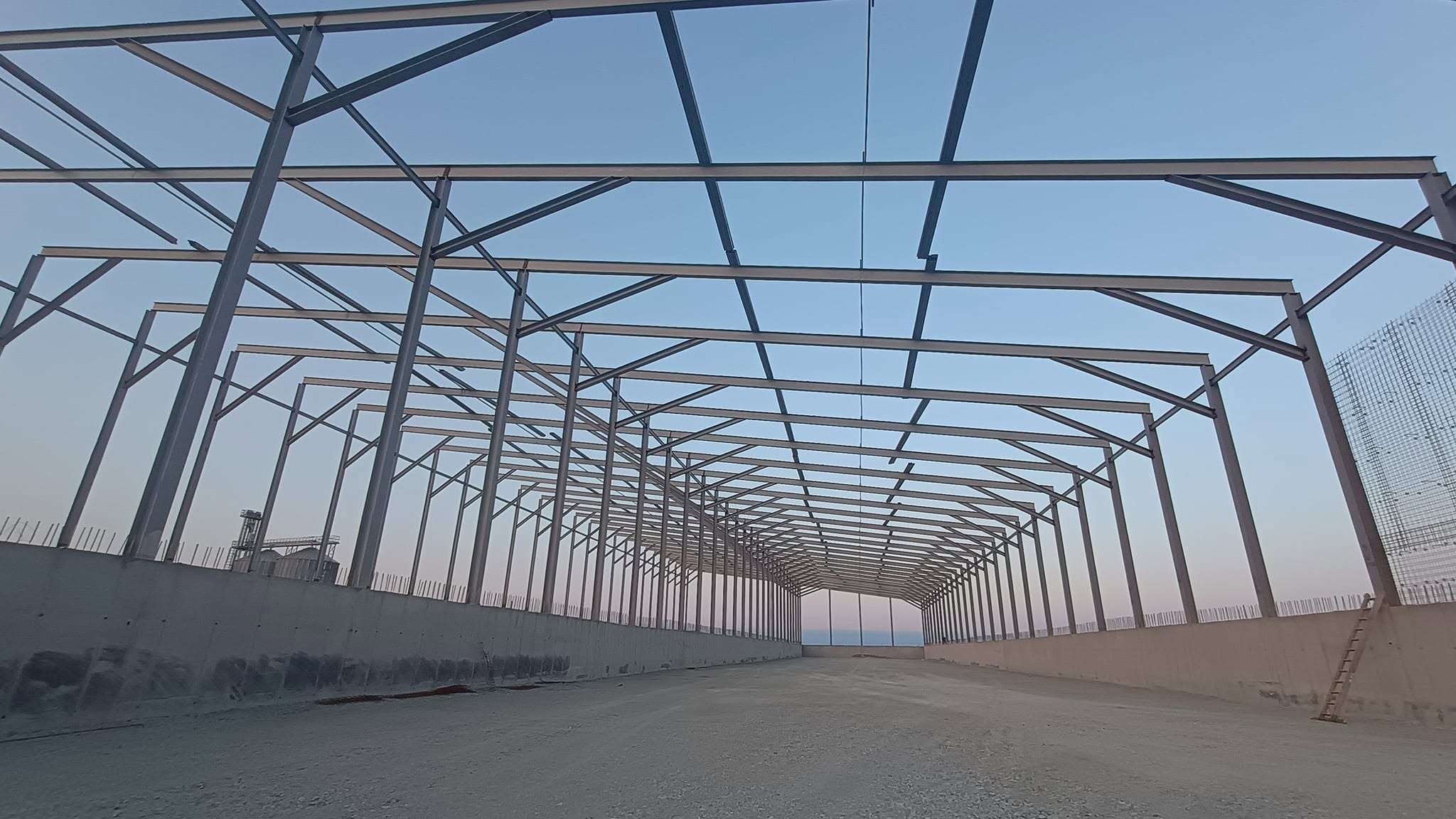 Perspectivă lungă printr-o hală în construcție, cu pardoseală de beton turnată