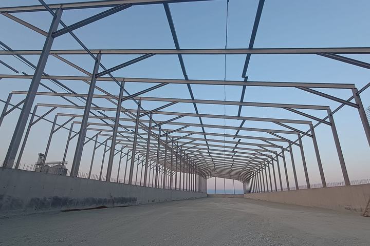 Perspectivă lungă printr-o hală metalică în construcție, cu pereți din beton