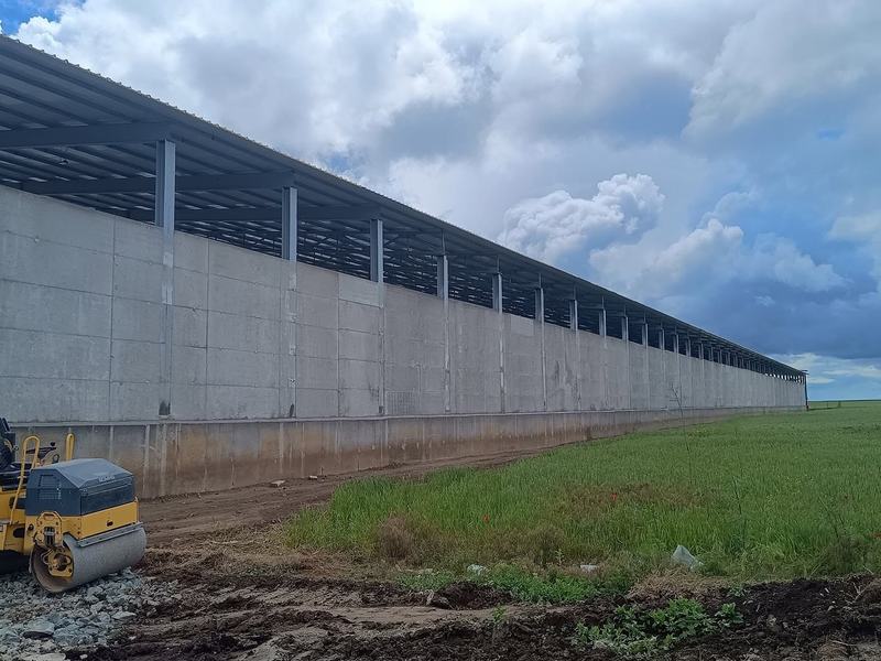 Hală lungă cu pereți din beton prefabricat, lângă un câmp verde