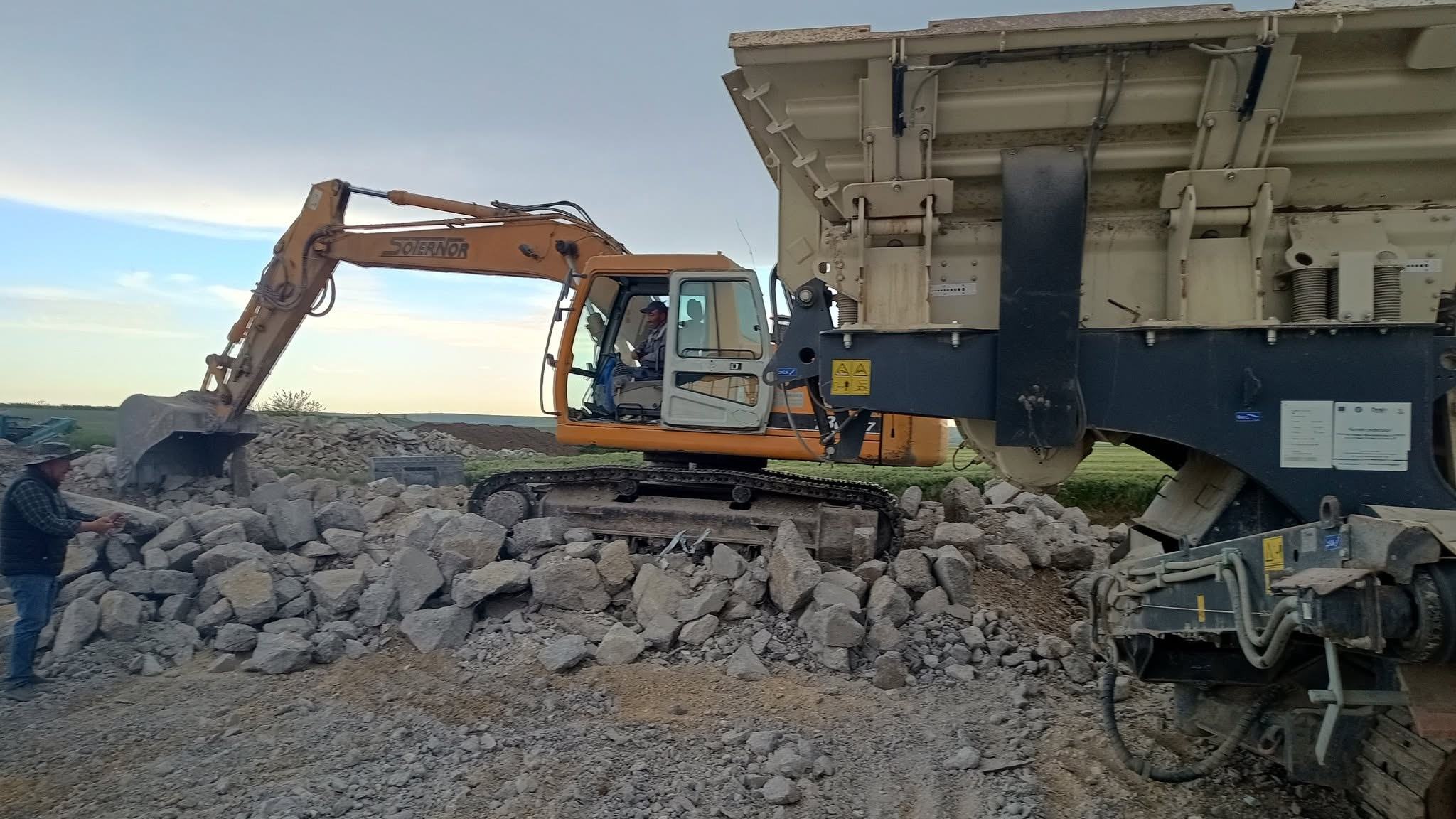 Excavator alimentând un concasor mobil cu beton din demolare