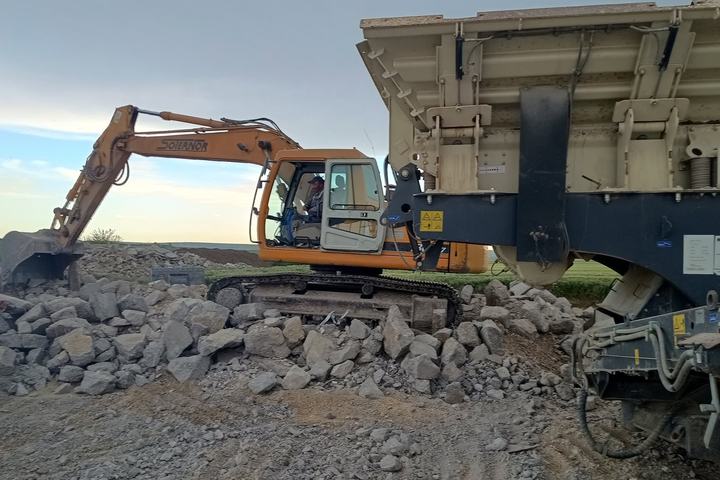 Excavator alimentând un concasor mobil cu beton din demolare