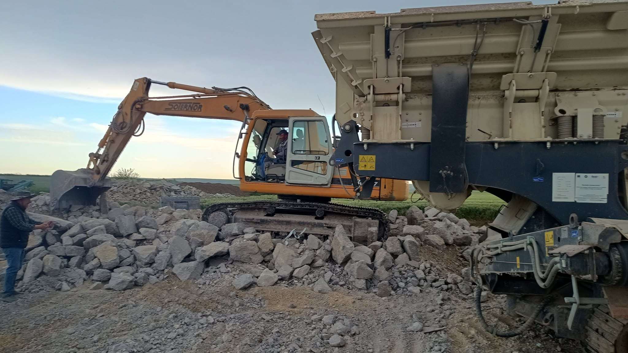 Excavator alimentând un concasor mobil cu beton din demolare