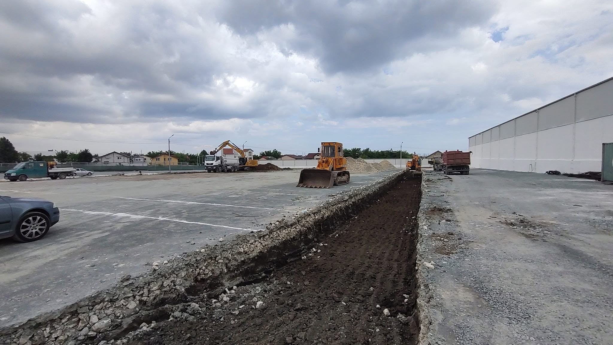Buldozer nivelând o platformă de pământ lângă o hală