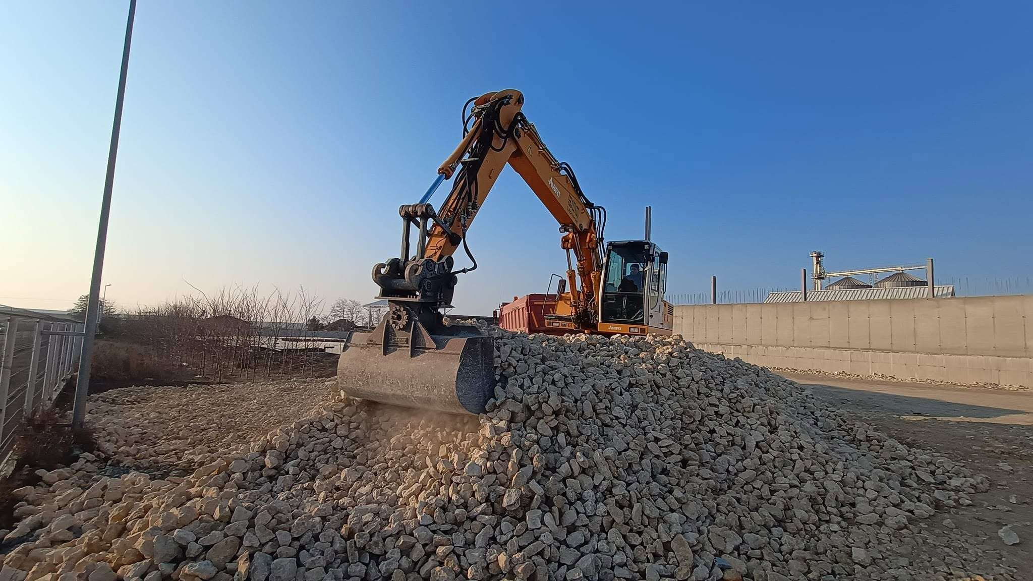 Excavator încărcând pietriș într-o autobasculantă, în lumina serii